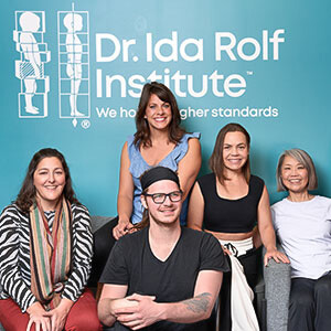 Small group of students and teacher seated and smiling in the lobby of the Dr. Ida Rolf Institute, taking a break from their Rolf Movement certification course.